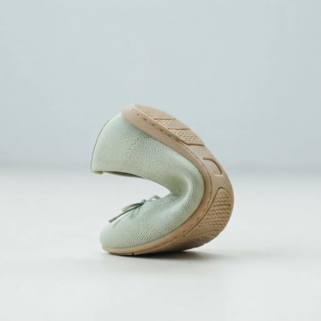 A flexible ballet flat bent to show its sole on a pale studio surface
