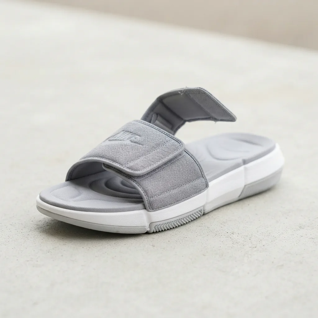 A gray men's Nike Offcourt Adjust slide sandal with its strap opened on a light surface