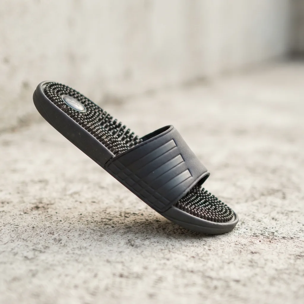 A dark men's adidas Adissage slide sandal showing its nubbed footbed on light concrete